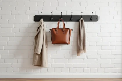 Porte-manteau mural en métal noir mat fixé sur un mur en brique blanche avec manteau et sac en cuir accrochés